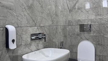 A bathroom with a marble wall, a white sink, a toilet, a hand dryer, and a towel rack.