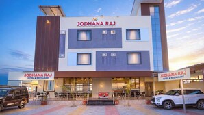 Un hôtel moderne doté d’un toit plat, de nombreuses fenêtres et d’une enseigne indiquant « HÔTEL ET RESTAURANT JODHANA RAJ ».