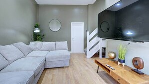 Een moderne woonkamer met een hoekbank, een wandgemonteerde televisie, een houten salontafel en een trap.