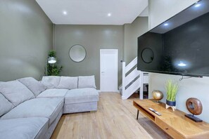 Ein modernes Wohnzimmer mit einem Ecksofa, einem Wand-Fernseher, einem Holztisch und einer Treppe.