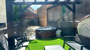 Een achtertuin met terras, een jacuzzi, kunstgras en tuinmeubilair.