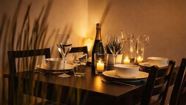 Mesa posta com pratos, copos, garrafa e velas.