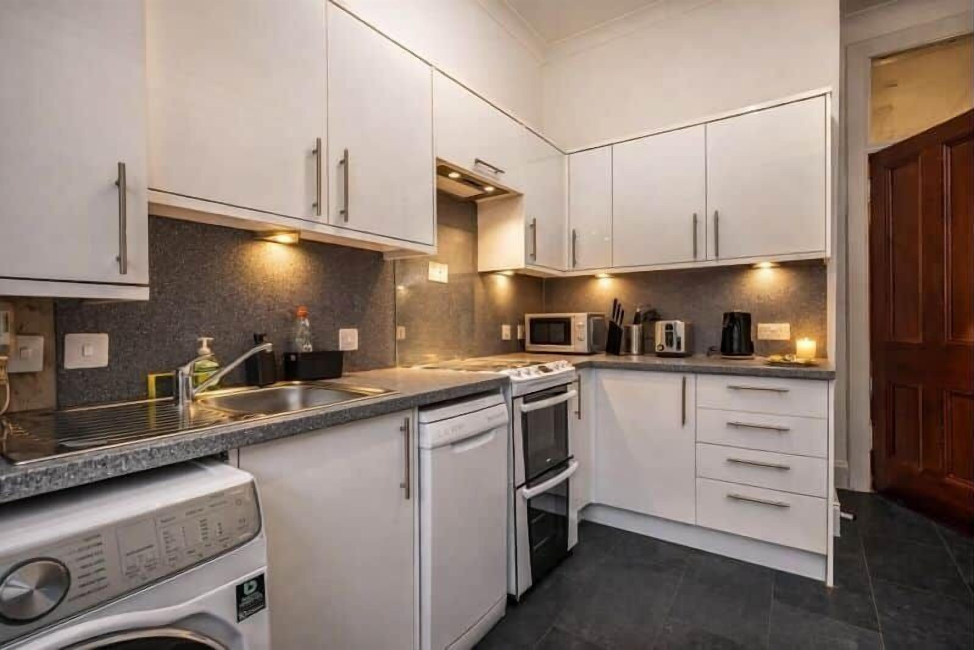A compact kitchen with white cabinets, a built-in oven, a microwave, and a washing machine.