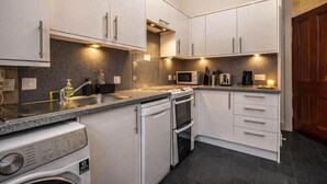Uma cozinha compacta com armários brancos, forno embutido, micro-ondas e máquina de lavar.