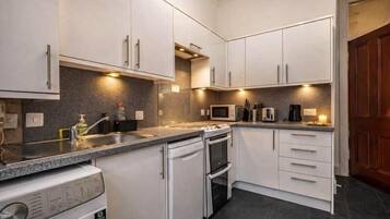 A compact kitchen with white cabinets, a built-in oven, a microwave, and a washing machine.