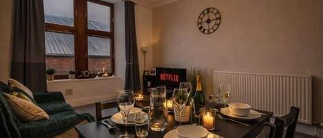 A dining area with a table set for two, a clock on the wall, and a Netflix sign.