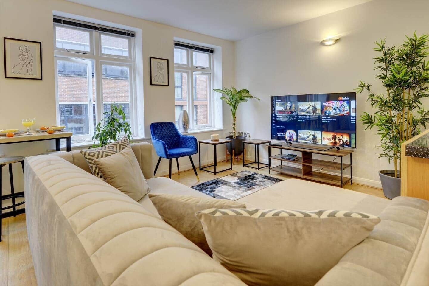 Een moderne woonkamer met een bank, een blauwe stoel, een televisie en een eethoek met een tafel en stoelen.