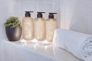 A bathroom with three bottles of conditioner, a potted plant, and a rolled towel on a white countertop. - Park 3 Bedroom House|4 Beds|Sleeps 6 Guests| Birmingham (Smethwick)