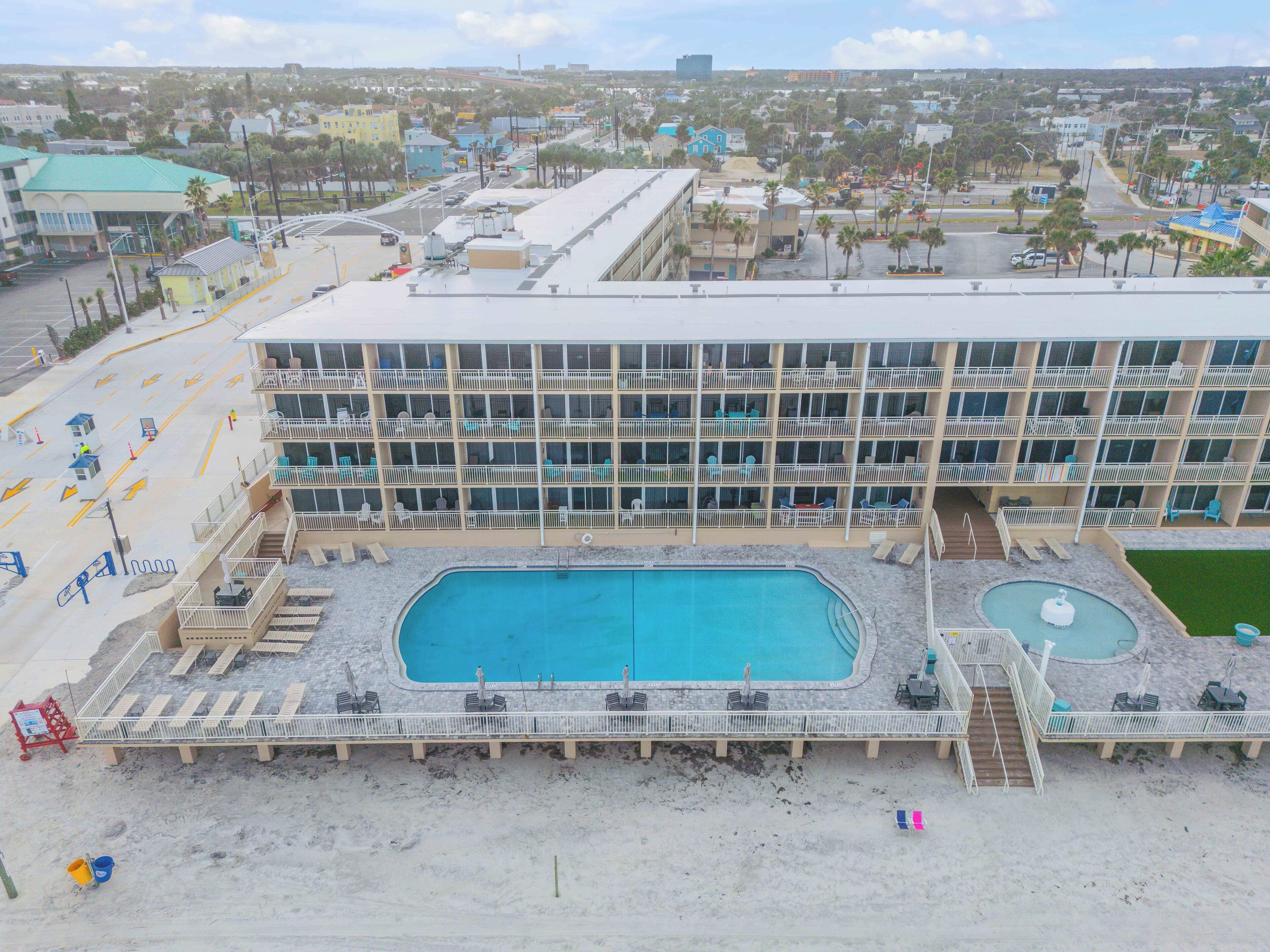 A hotel with a large pool, multiple balconies, and a view of the surrounding cityscape.