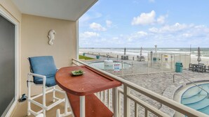 Ein Balkon mit Blick auf den Strand, ein Stuhl, ein kleiner Tisch und ein Schwimmbecken.