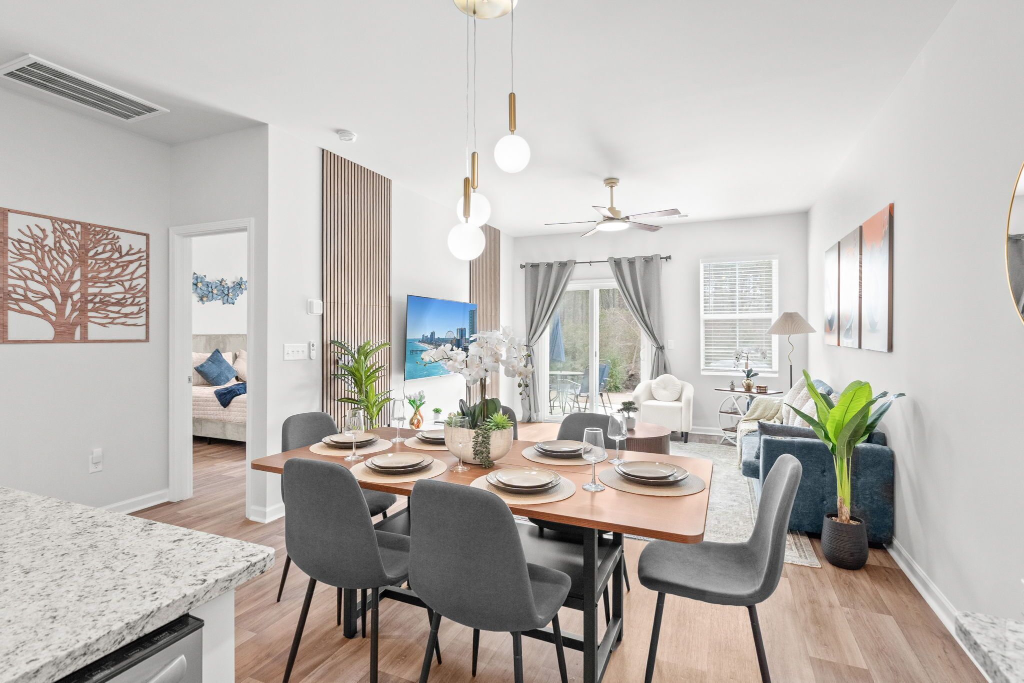 A modern dining area with a wooden table set for four, surrounded by grey chairs.