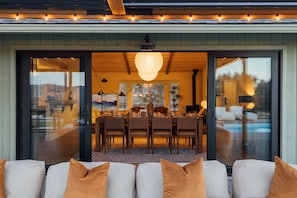 Uma área de refeições com uma mesa posta para quatro pessoas, uma janela grande e vista para uma piscina.