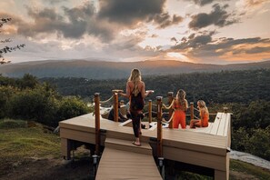 Um deck de madeira com vista para uma paisagem montanhosa ao pôr do sol.