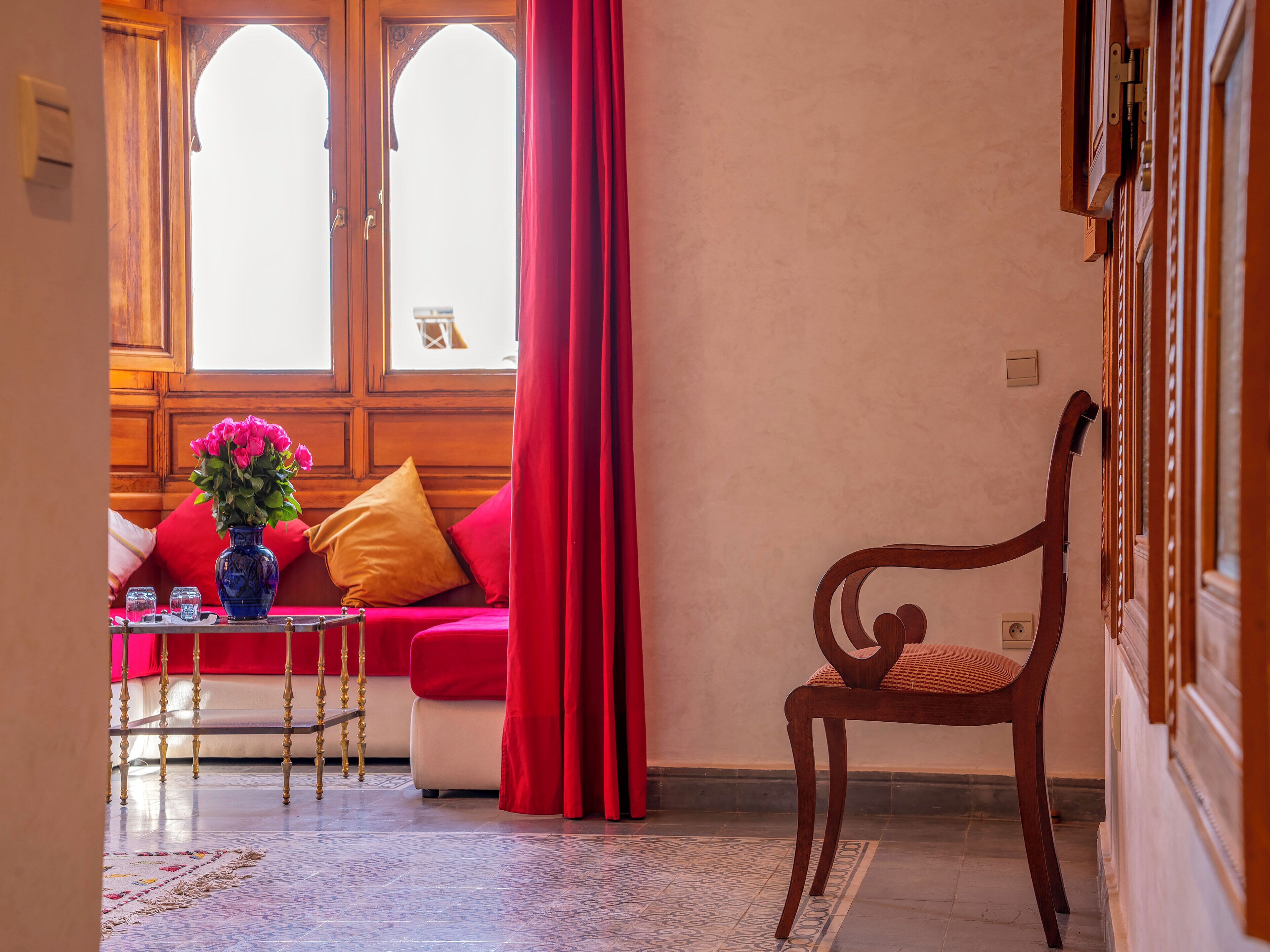 A room with a wooden bench, a red sofa, a vase with flowers, and a window with curtains.