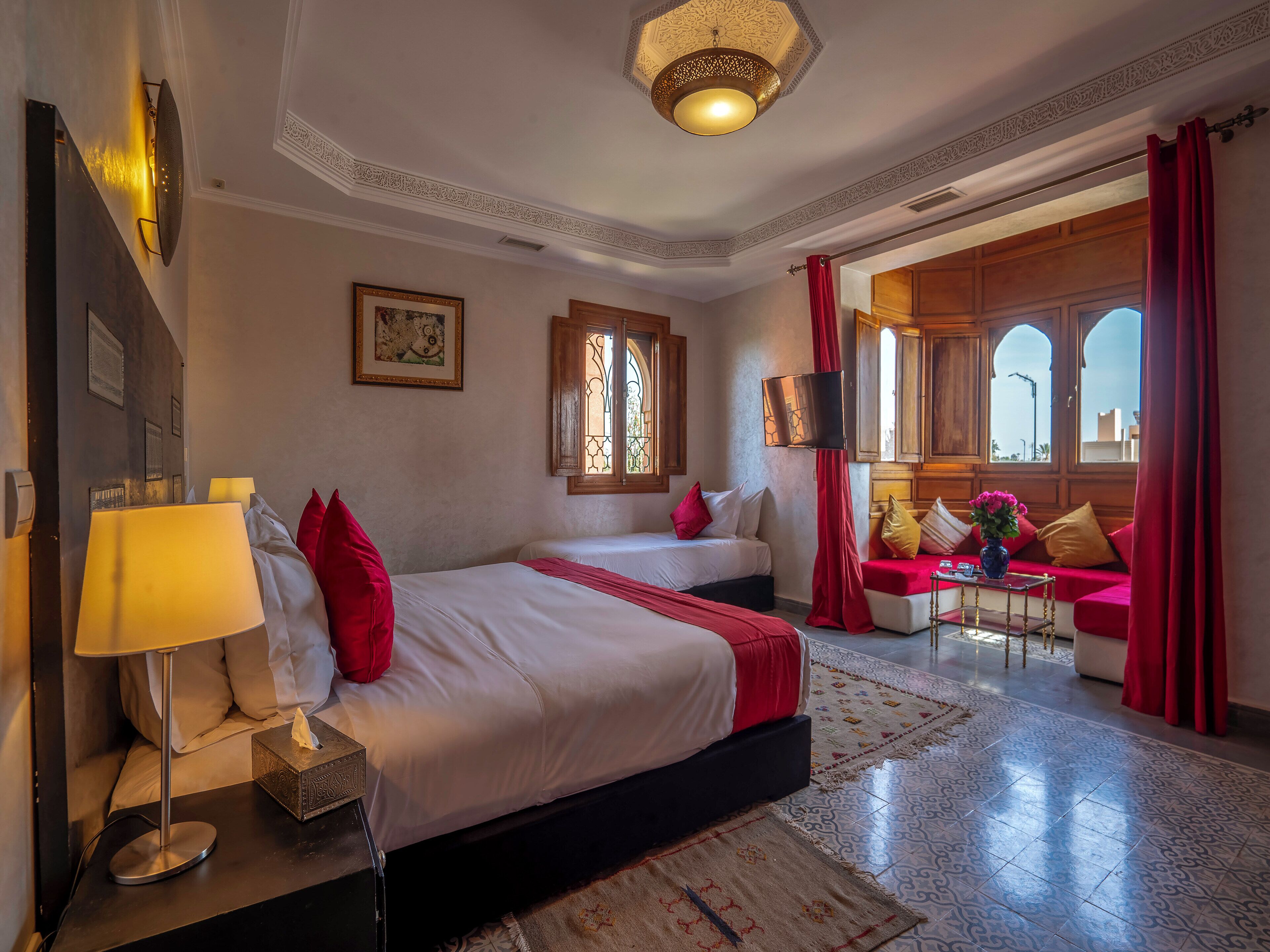 Habitación de hotel con dos camas, zona de estar con sofá, ventana grande y candelabro.