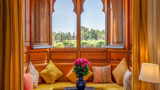 Une pièce avec un banc en bois, un vase de fleurs et une vue sur un terrain de golf, visible à travers des fenêtres en arc de cercle.