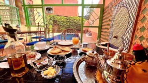 Une table à manger dressée avec de la vaisselle de style marocain, comprenant une théière, un pichet et un plateau avec du pain et des olives.