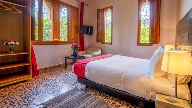A bedroom with a bed, a chair, a TV, and a window with a view of greenery. - Hotel Boutique RAM Spa (Marrakech)