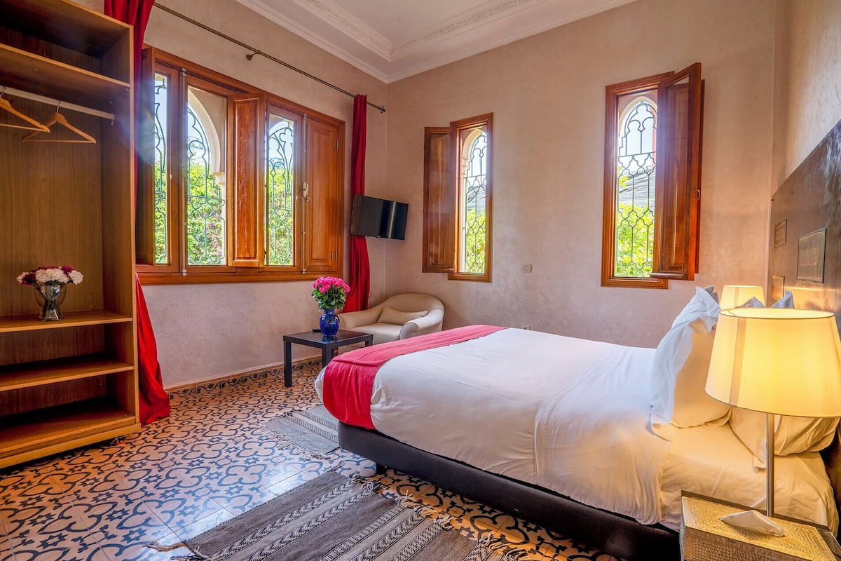 A bedroom with a bed, a chair, a TV, and a window with a view of greenery.