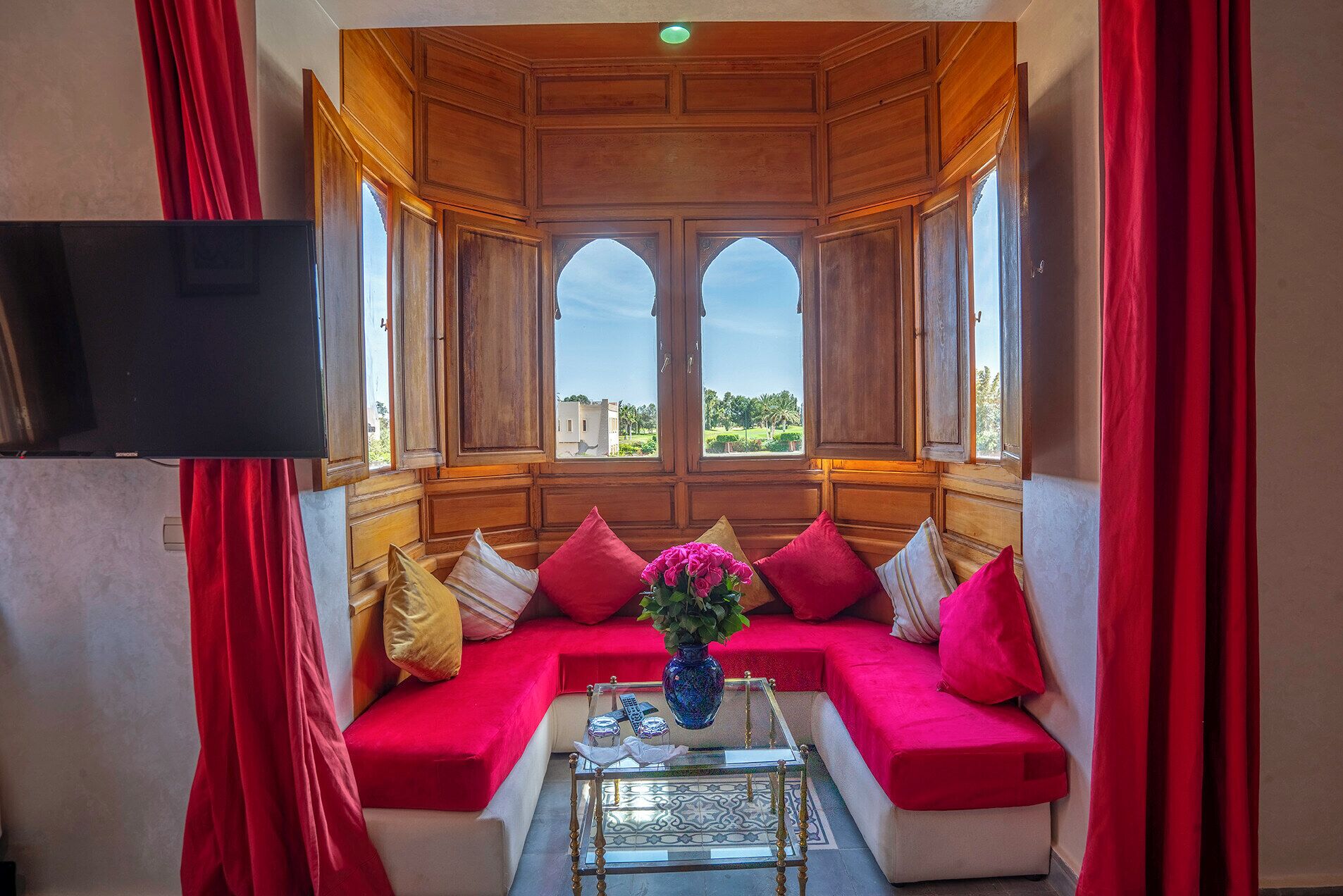 Une pièce avec un canapé rouge, une table basse en verre et un téléviseur fixé au mur.