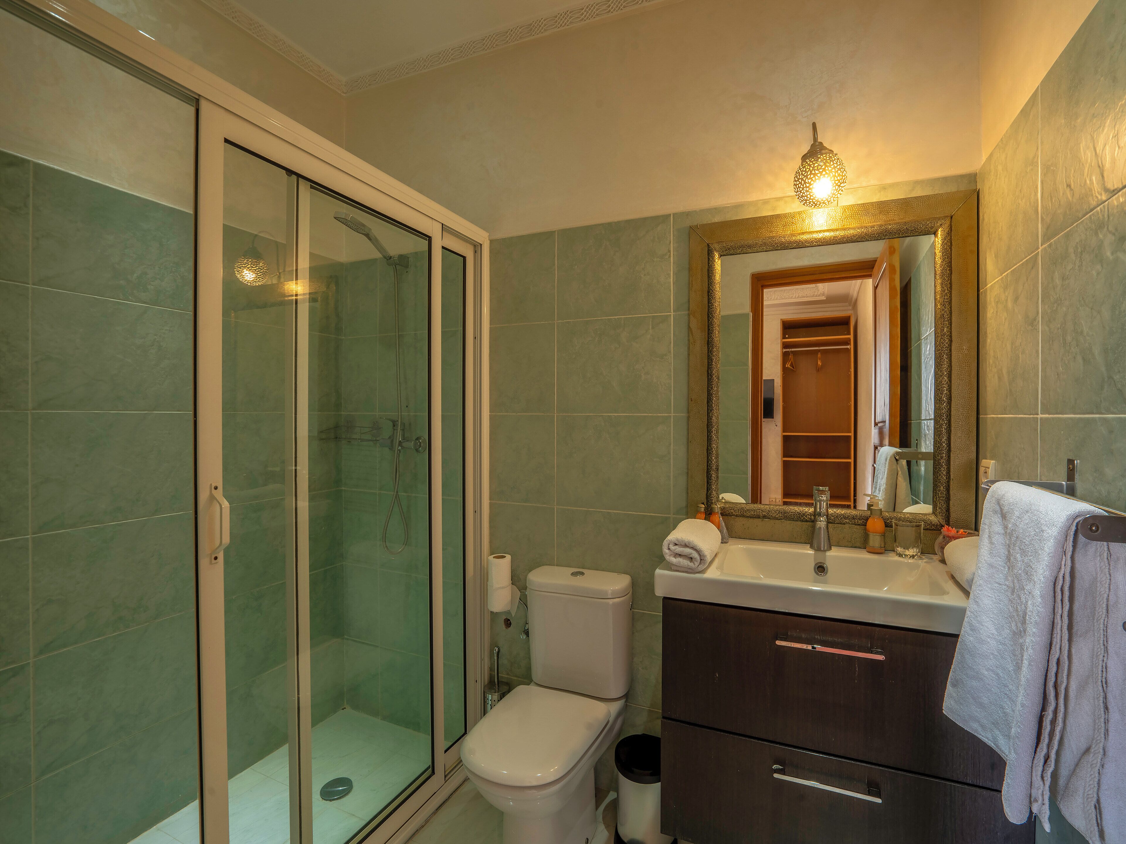 Un baño con ducha envuelta en vidrio, inodoro, lavabo y espejo con marco decorativo.