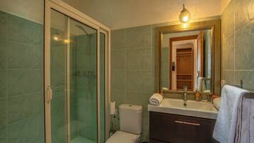 Un baño con ducha envuelta en vidrio, inodoro, lavabo y espejo con marco decorativo.