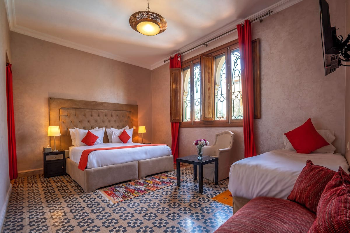 A hotel room with a large bed, a smaller bed, a chair, a table, and a decorative vase.