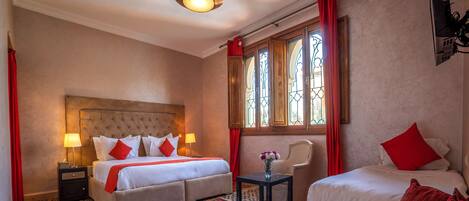Habitación de hotel con una cama grande, una cama más pequeña, una silla, una mesa y un jarrón decorativo.