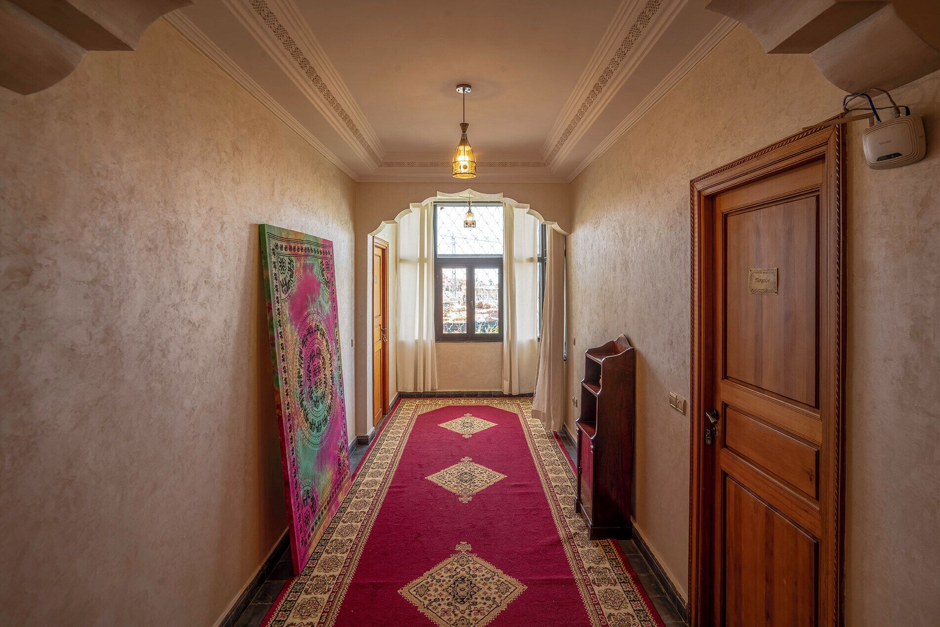 A hallway with patterned carpet, a wooden door, and a hanging light fixture.