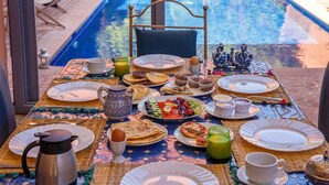 Une table de petit-déjeuner avec des assiettes, des tasses et un pichet, placée au bord d’une piscine, avec vue sur l’eau.