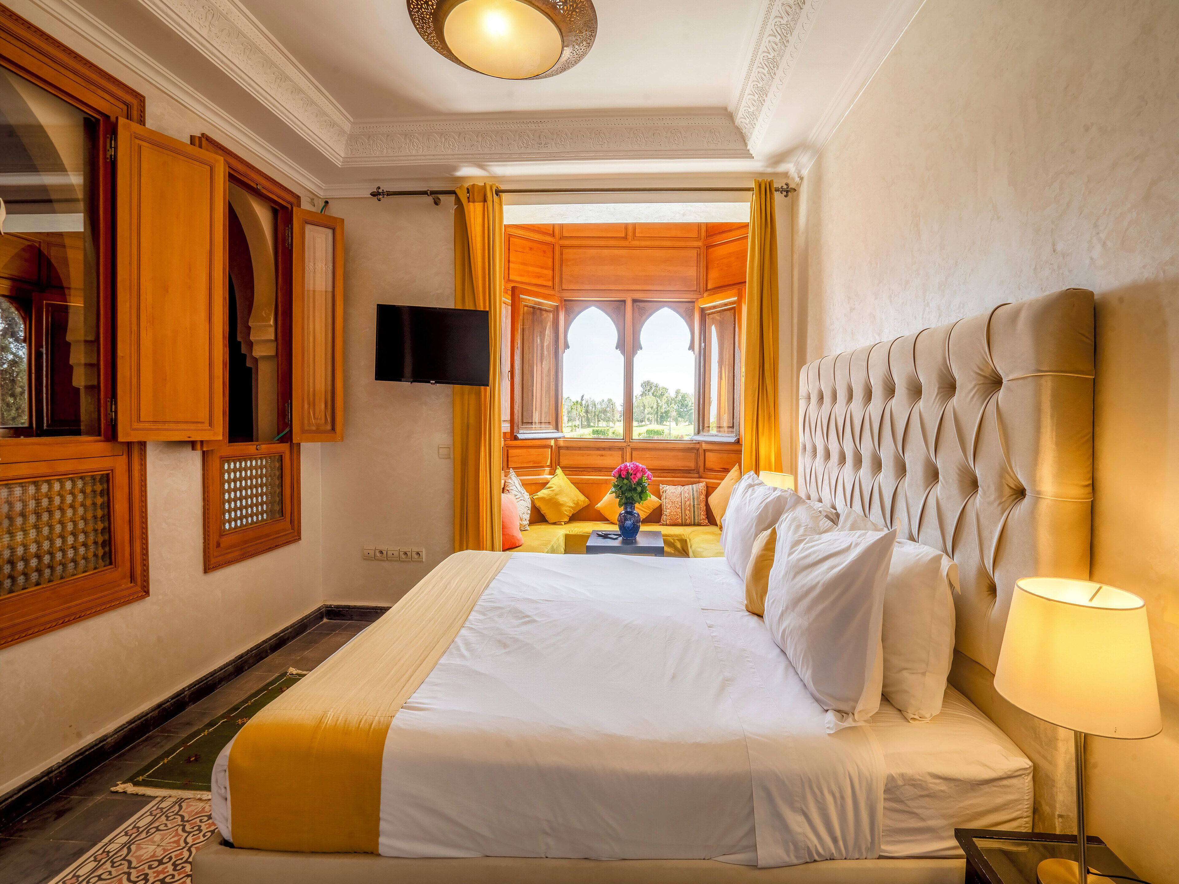 Ein Hotelzimmer mit einem großen Bett, einem Fernseher und Blick ins Freie durch bogenförmige Fenster.