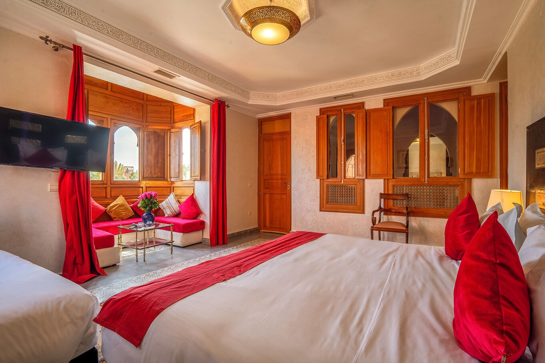 A hotel room with a large bed, a sofa, a TV, wooden cabinets, and a window with curtains.