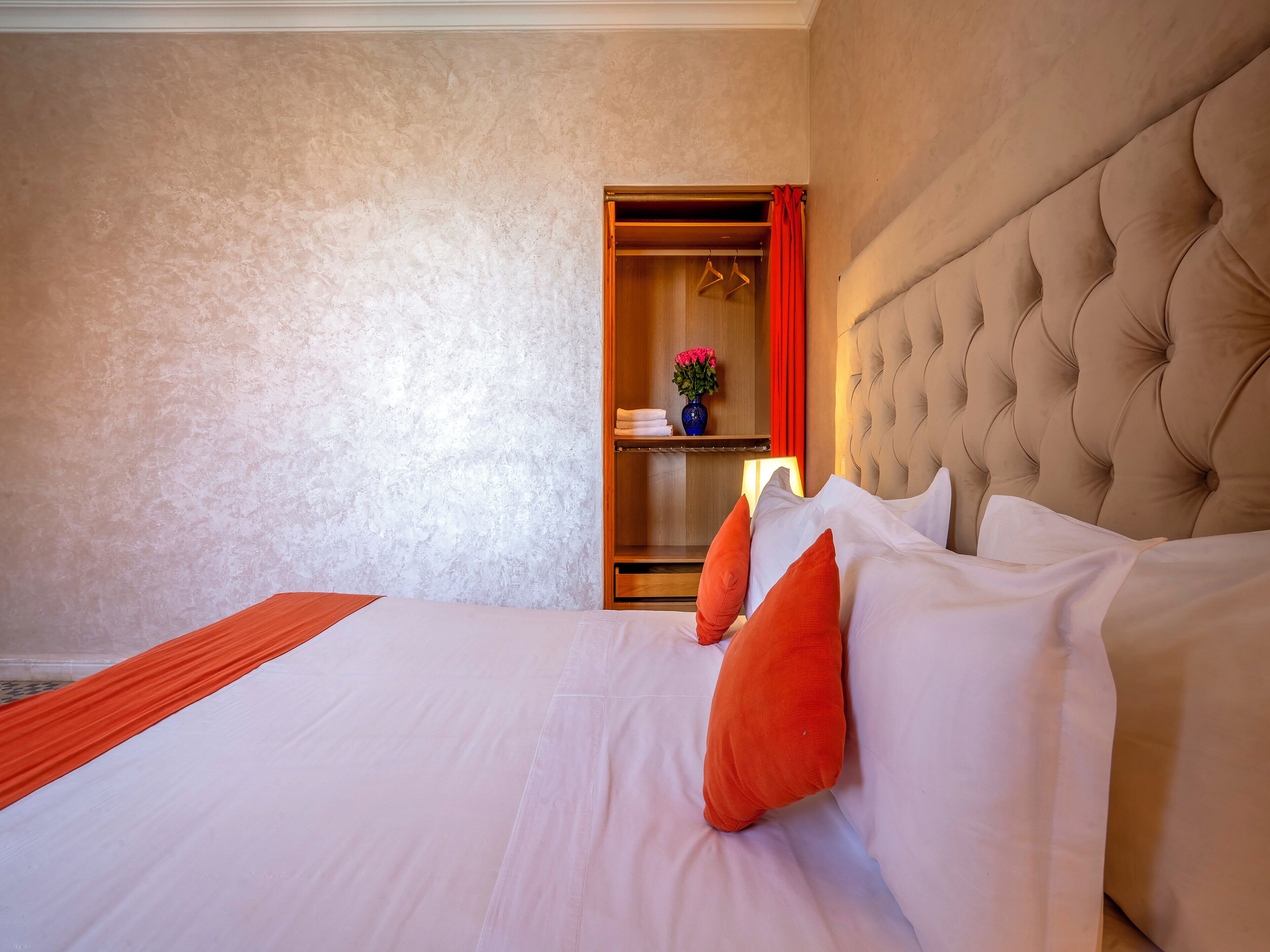 A hotel room with a large bed, a wooden wardrobe, and a red curtain.