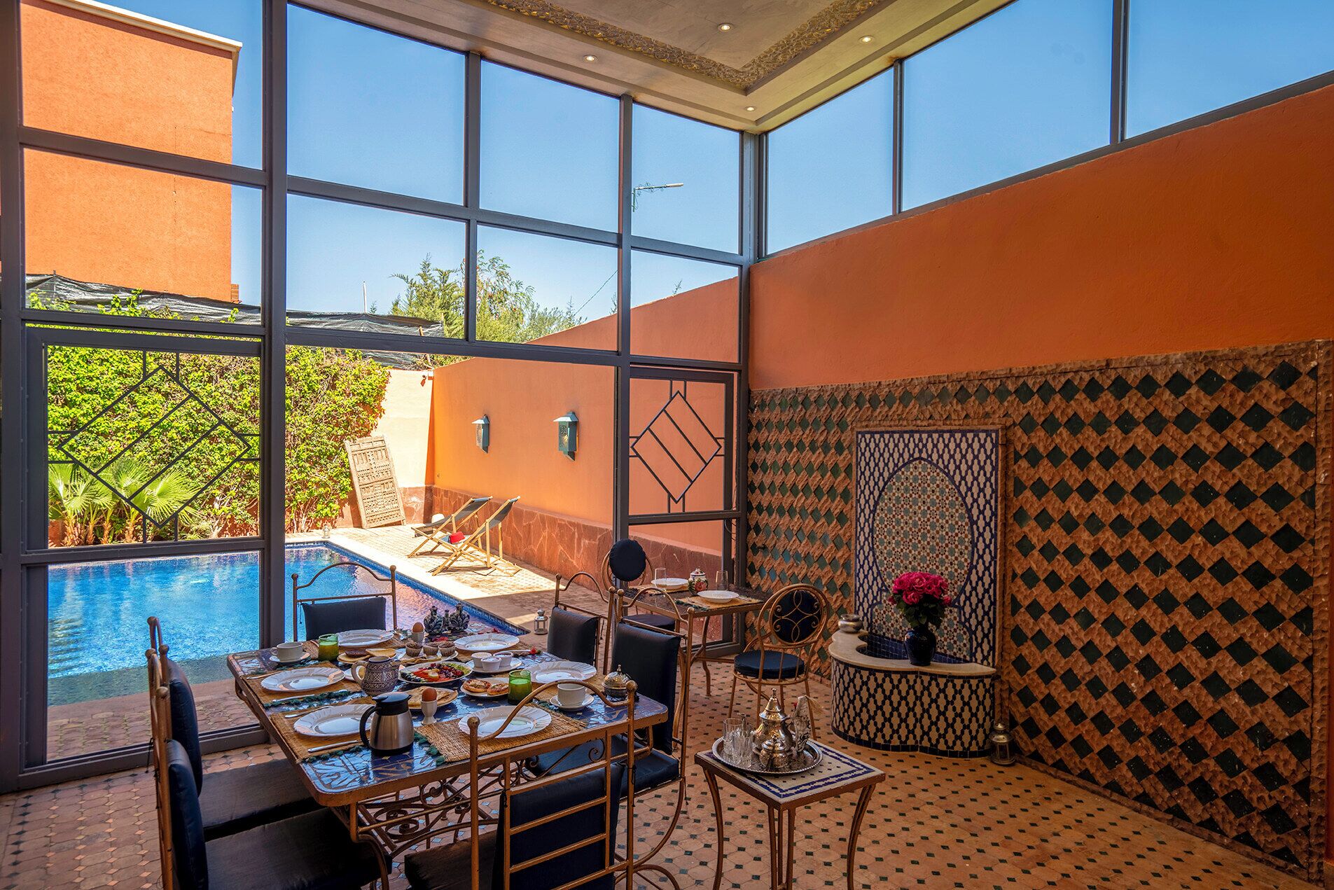 A dining area with a pool view, a table set for a meal, and a decorative wall with a geometric pattern.