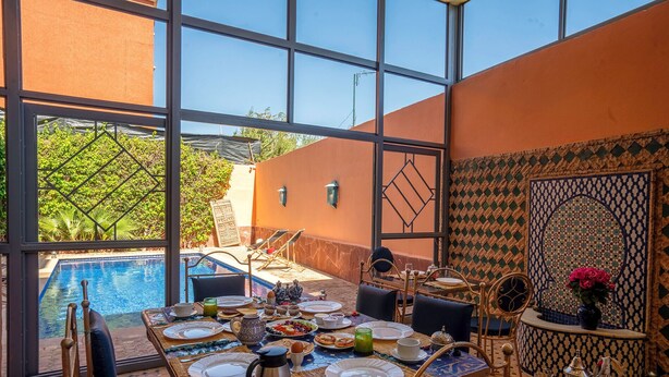 Un coin repas avec vue sur la piscine, une table dressée pour le repas et un mur décoratif.