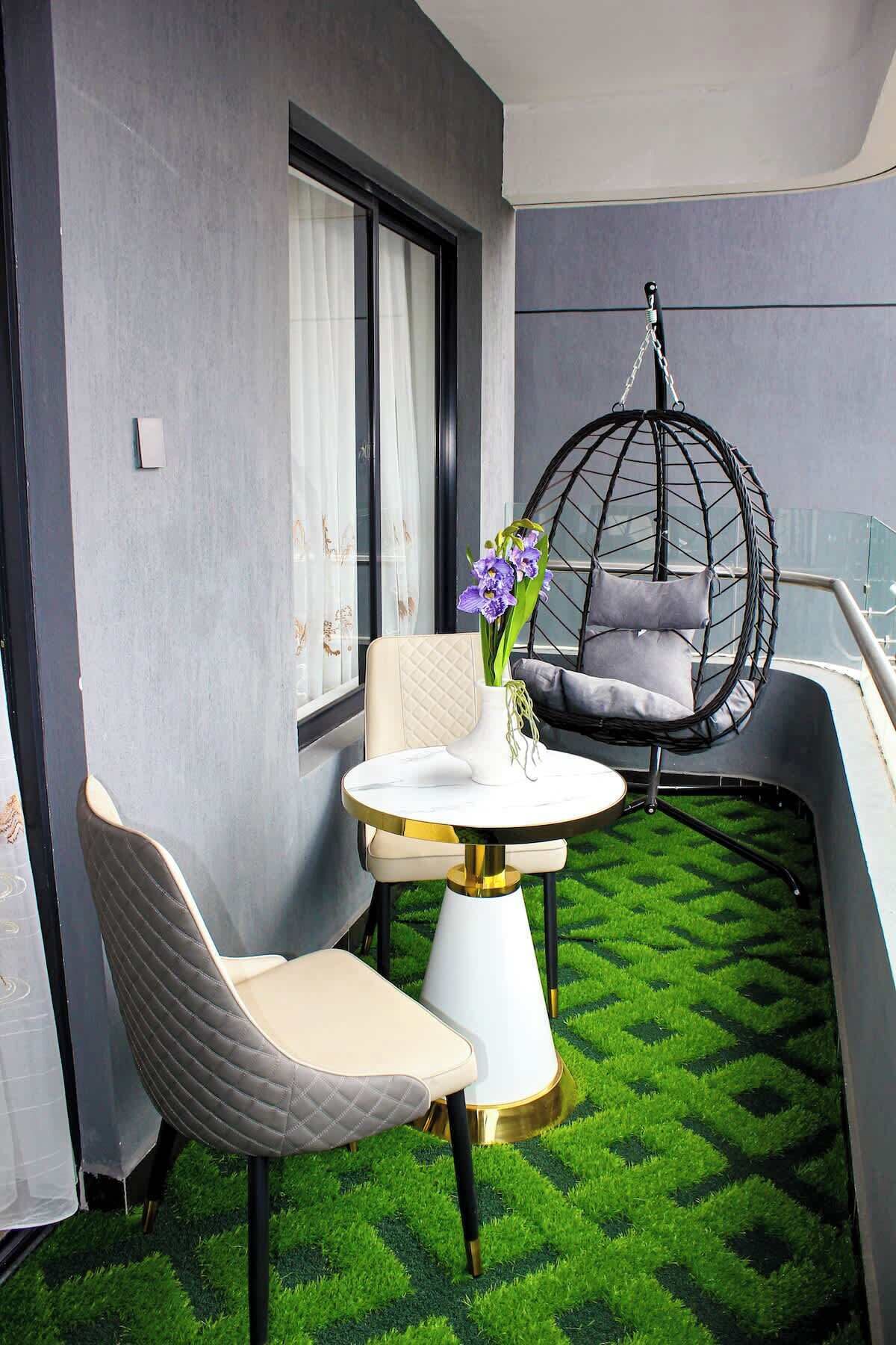 A balcony with a round table, two chairs, a hanging chair, and a vase with flowers.