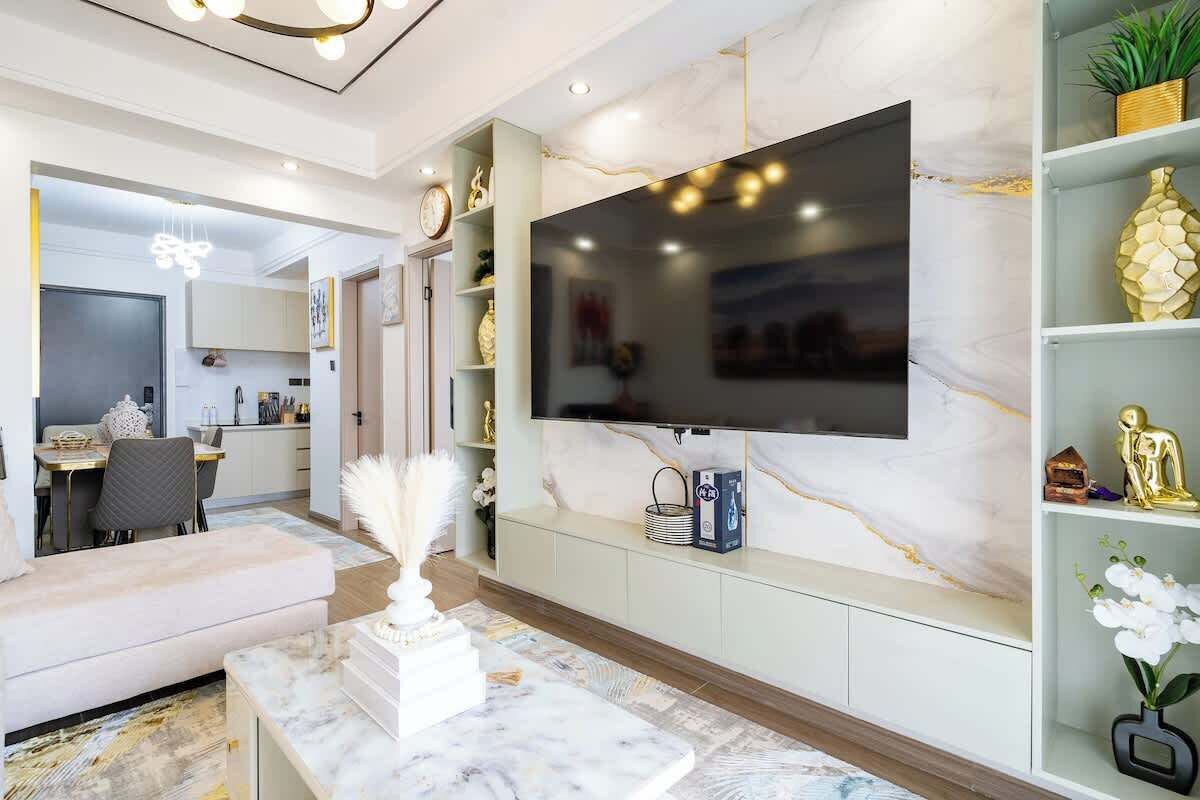Una sala de estar moderna con un televisor de pantalla plana grande montado en una pared de mármol, un sofá, una mesa de centro y un comedor al fondo.