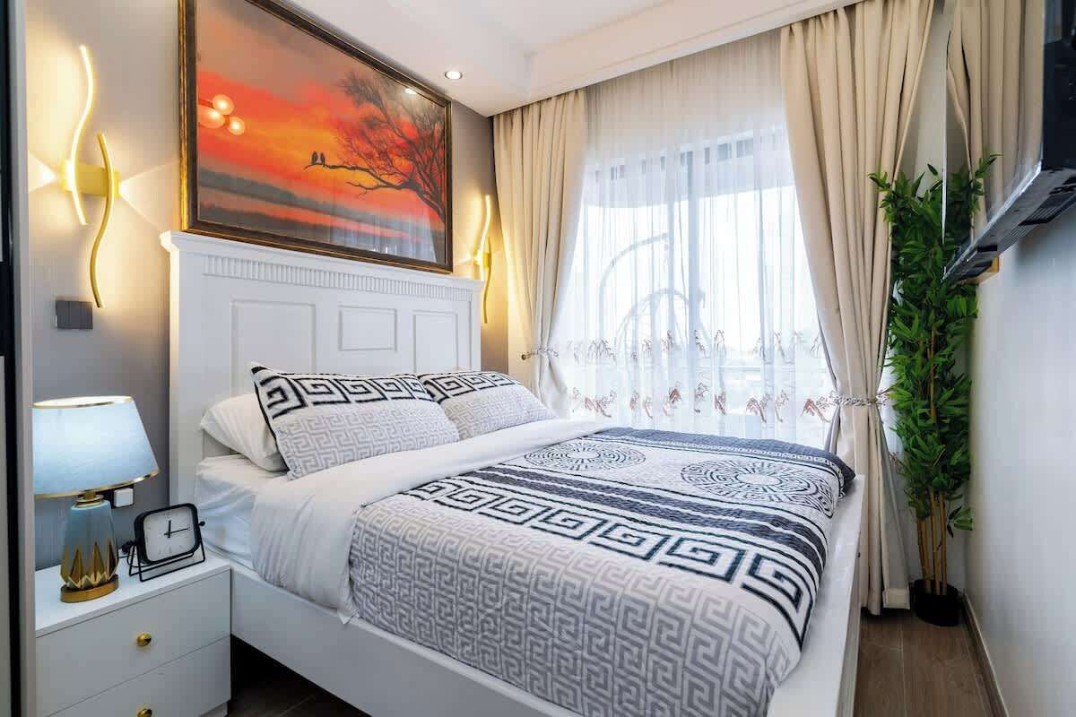 Une chambre bien rangée, avec un lit, une table de chevet, une lampe et un tableau accroché au mur.