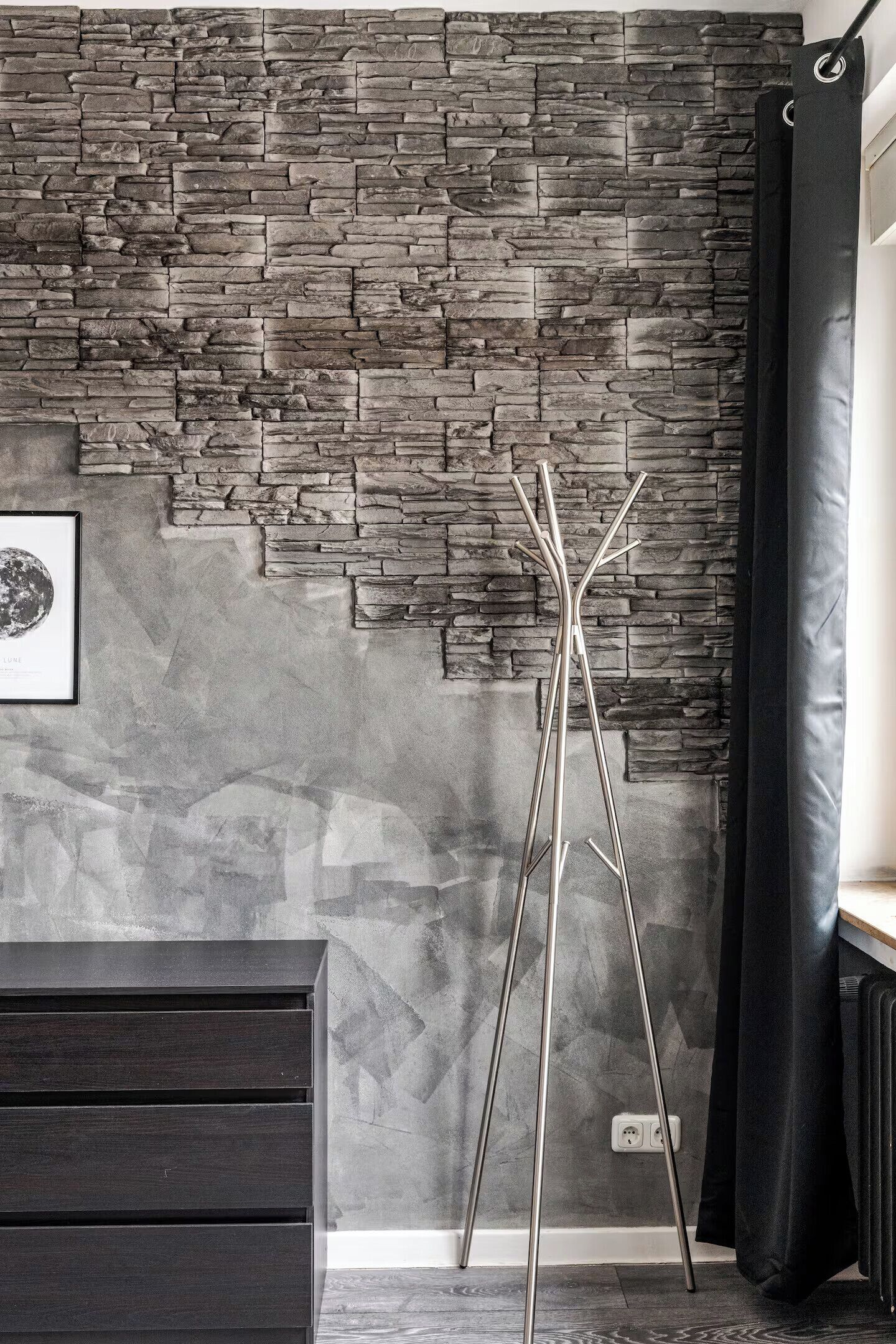 A room with a stone wall, a framed picture, a tall metal stand, and a dark-colored cabinet.
