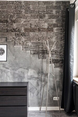 Een kamer met een stenen muur, een ingelijst schilderij, een hoge metalen standaard en een donker kast.
