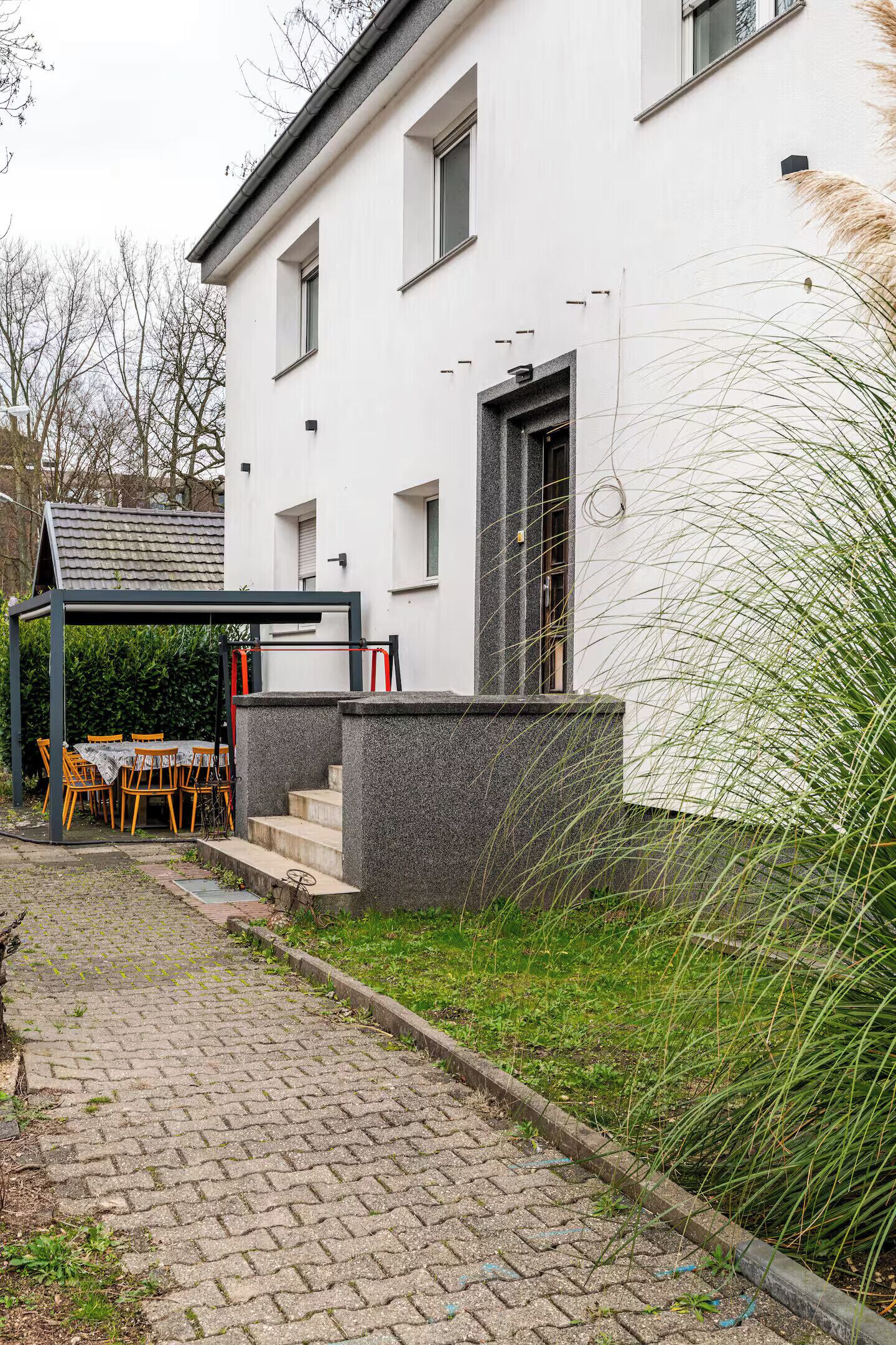 Een modern huis met een verharde oprit, een overdekt terras en een stenen muur.