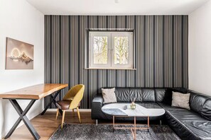 Een moderne woonkamer met een zwarte leren bank, een houten salontafel, een gele stoel en een gestreepte wand.