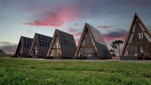 A row of modern, triangular-shaped buildings with large windows and solar panels, set against a sunset sky. - Mont Hermon Hotel Castro (Castro)