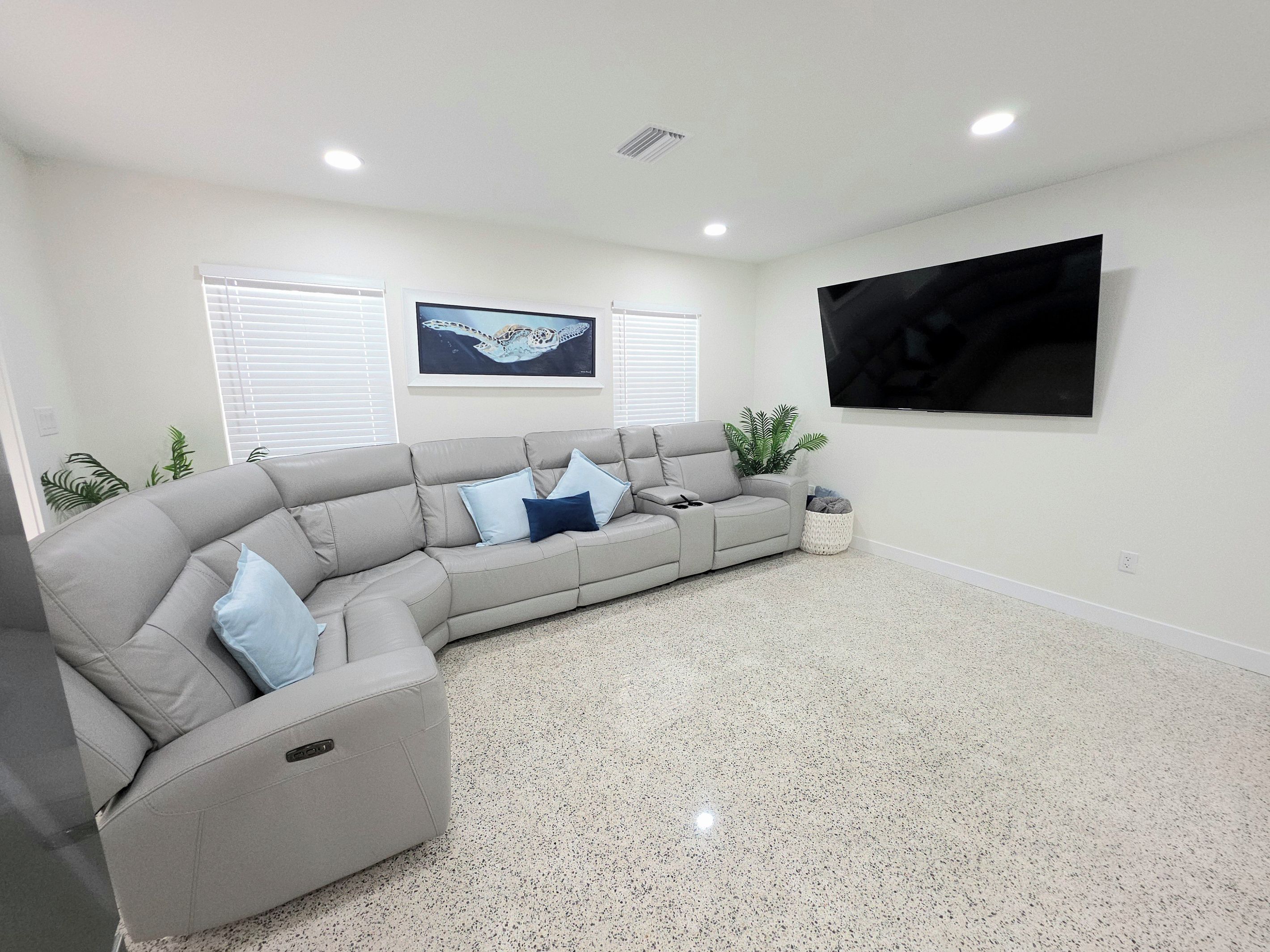 Uma sala de estar moderna com um sofá seccional cinza, uma TV de tela plana fixada na parede e um piso salpicado.