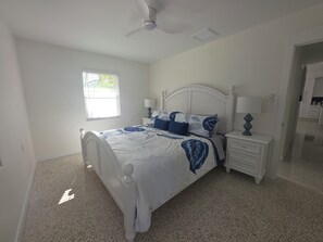 Ein Schlafzimmer mit einem Bett, Nachttischen, einem Deckenventilator und einem Fenster.