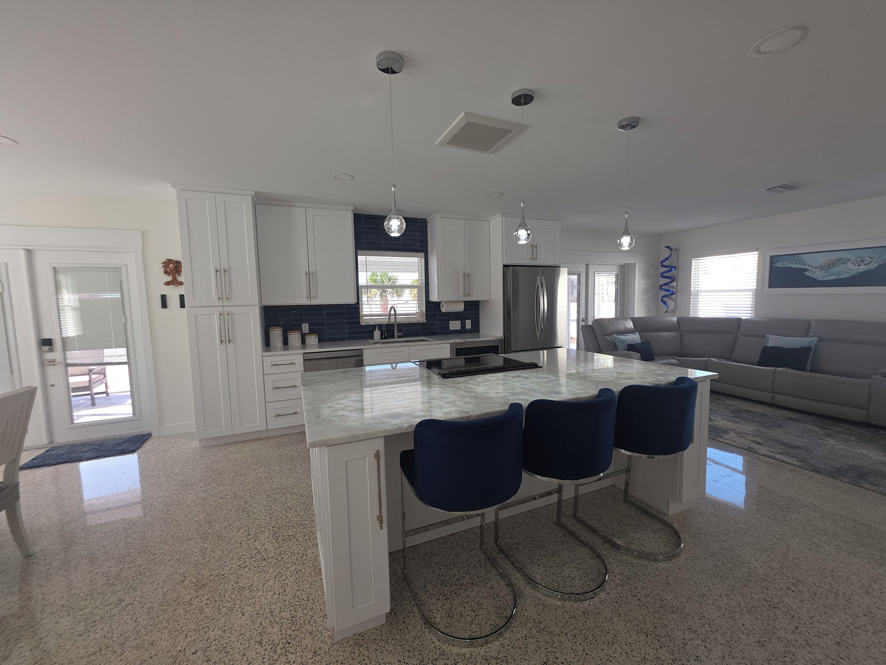 A modern kitchen with white cabinets, a central island with bar stools, stainless steel appliances, and pendant lighting.