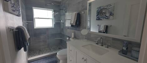 Un baño moderno con cabina de ducha de vidrio, inodoro, lavamanos con espejo y perchero para toallas.