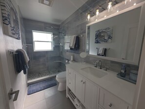 Ein modernes Badezimmer mit Duschkabine aus Glas, einem weißen Waschbecken und einem großen Spiegel.