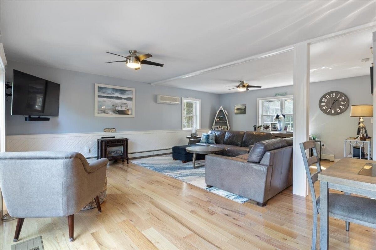 A spacious living room with a grey sofa, a wooden coffee table, and a television mounted on the wall.