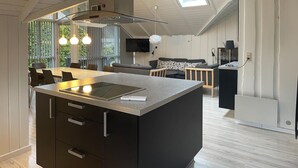 A modern kitchen with a central island, built-in appliances, and a dining area with a sofa and chairs. - Amazing home in Rørvig with sauna (Rørvig)